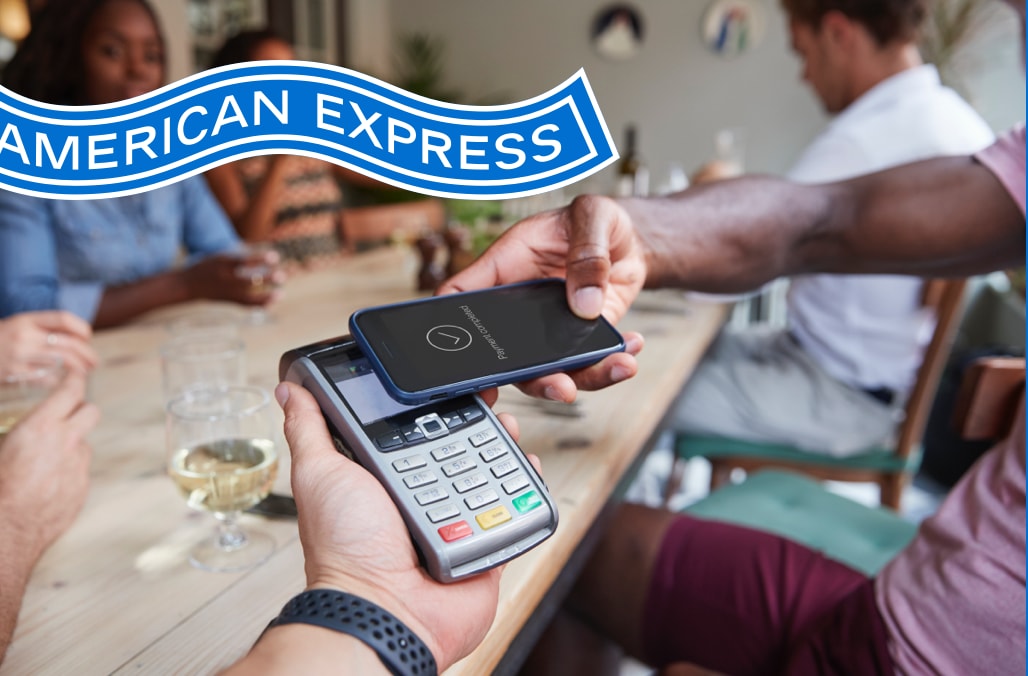 An Amex Member making a contactless payment with their mobile device while seated at a restaurant