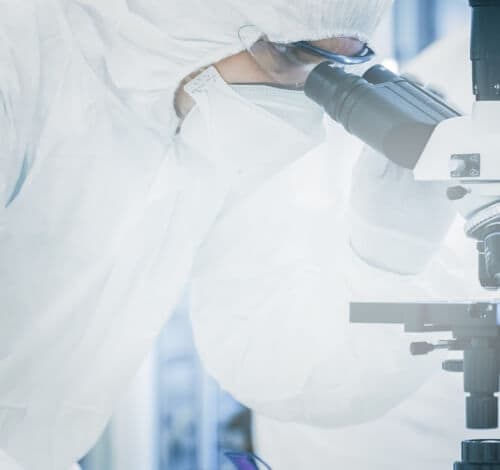 Man wearing lab coat and mask looking at microscope