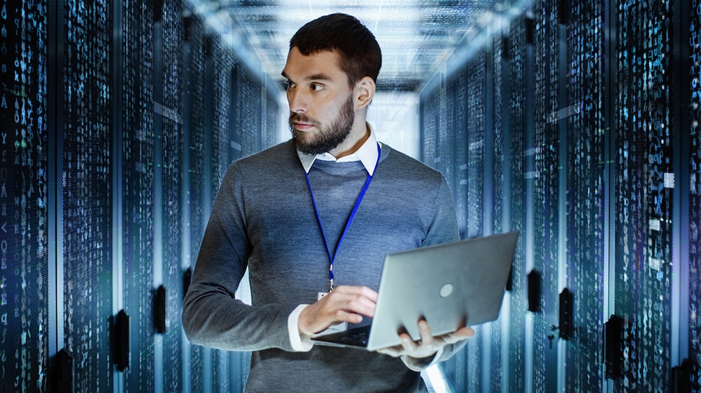 A man holding a laptop in a room full of systems - cloud computing technology