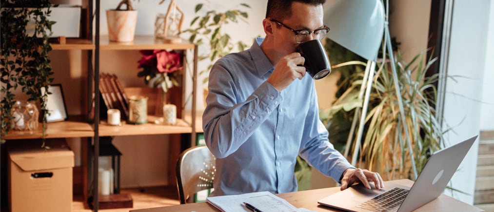 Businessman with paperwork using laptop and drinking coffee