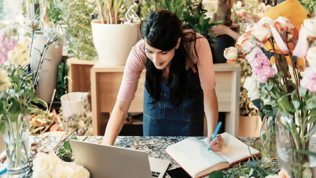 A photo of a woman using a laptop and writing, highlighting the benefit of blogging for business visibility and engagement.