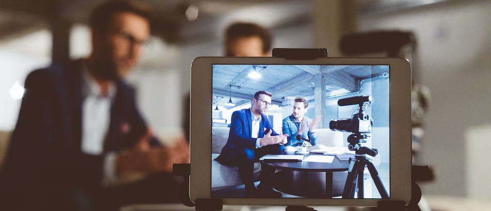 Two bloggers on digital tablet screen. Businessman with male guest recording a video blog on camera. Behind the scenes of a business vlog. (Two bloggers on digital tablet screen. Businessman with male guest recording a video blog on camera. Behind the