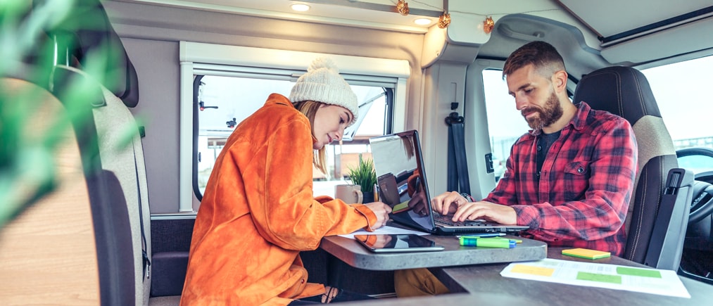 Ein Mann und eine Frau arbeiten remote in einem Wohnmobil am Laptop.