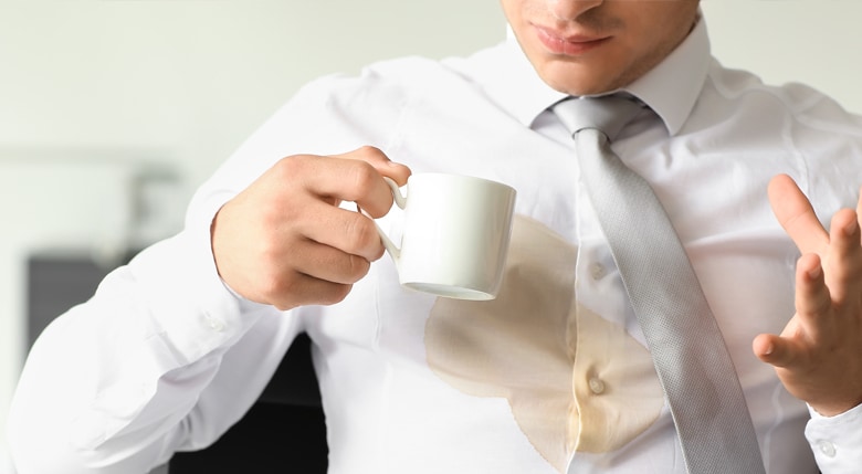 Ein junger Mann schüttet sich versehentlich Kaffee über sein weißes Hemd.