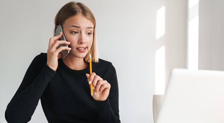Eine junge Frau mit verwirrtem Gesichtsausdruck macht sich beim Telefonieren Notizen.