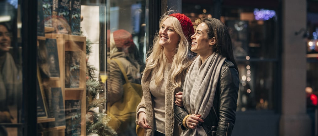 Zwei Frauen in winterlicher Kleidung stehen beim Shoppen vor einem Schaufenster.