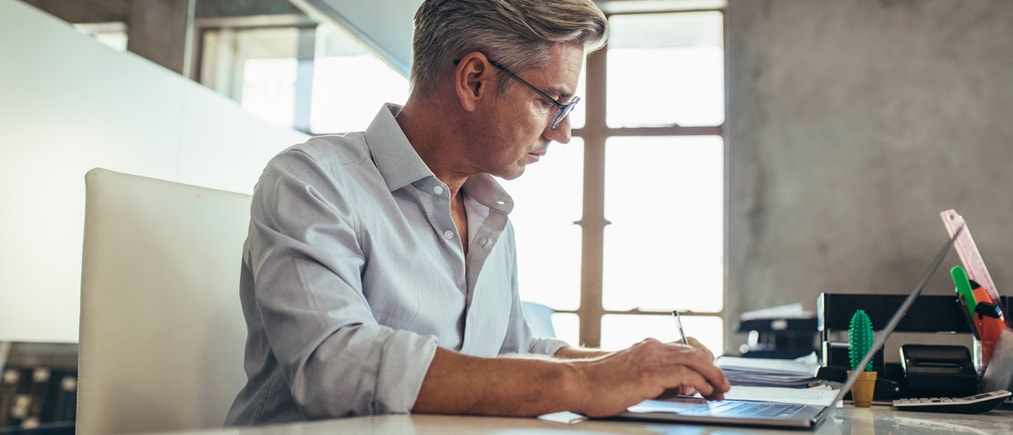 Mann mit Brille sitzt konzentriert im Büro und tippt auf seinem Laptop.