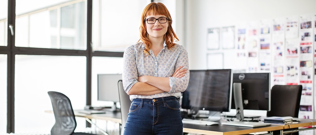 Portrait of confident young businesswoman standing with her arms crossed in office. Female professional in casual clothing looking at camera.