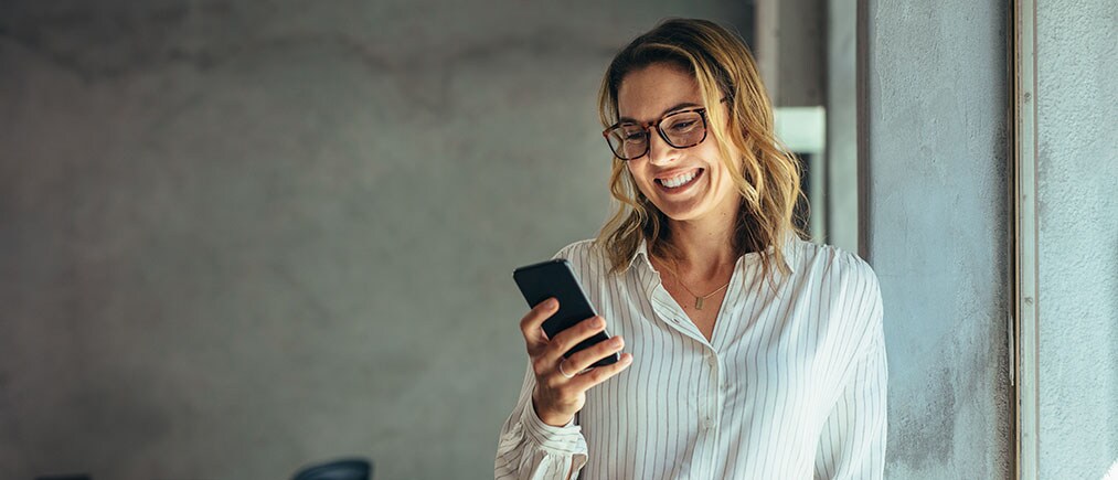 Smiling businesswoman using phone in office. Small business entrepreneur looking at her mobile phone and smiling.