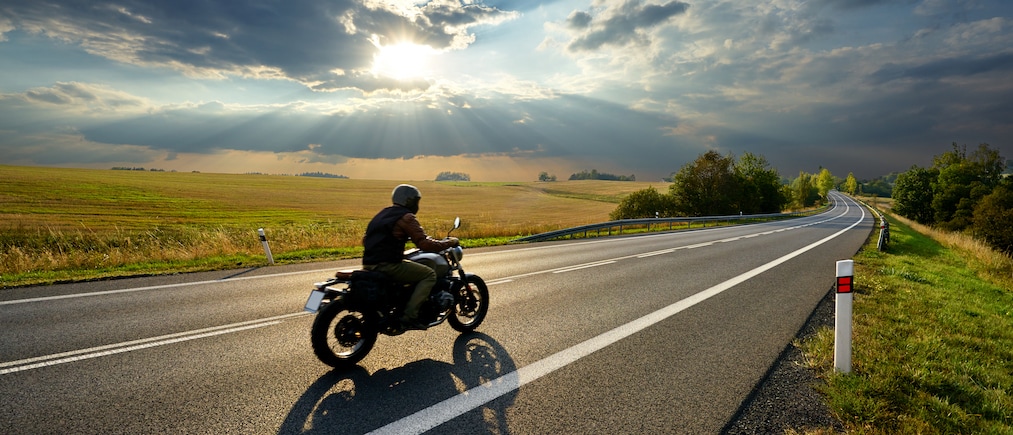 Motorcycle driving on the asphalt road in rural landscape at sunset with dramatic clouds