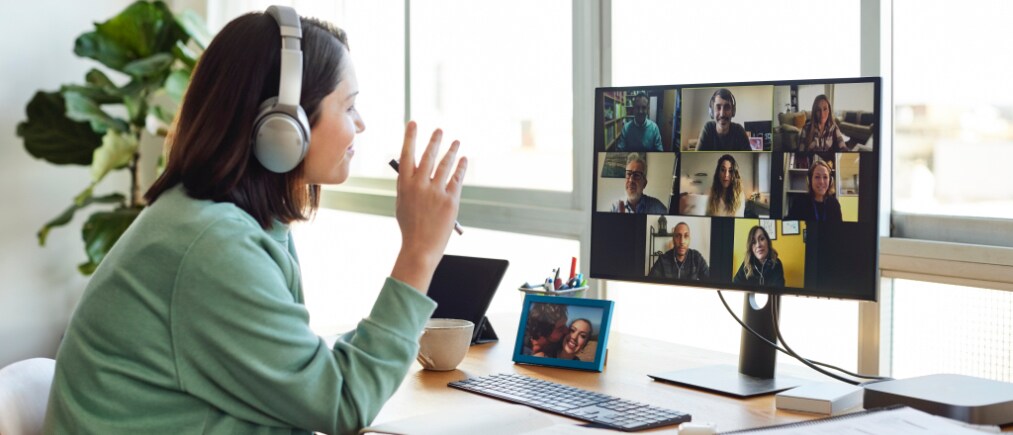 Female entrepreneur discussing with colleagues on video call. Businesswoman is sitting at table in home office. She is wearing headphones.