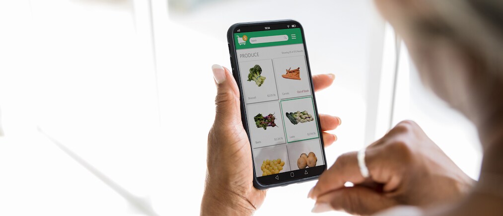 A woman uses a grocery delivery app on her smartphone. She is selecting fresh produce while using the app.