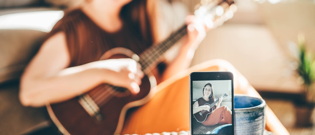 Selective focus on phone with video blogger playing on ukulele on phone screen.