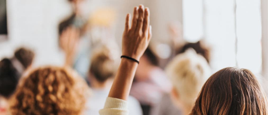 Rear view of casual businesswoman raising her arm to ask the question on education event in a board room.