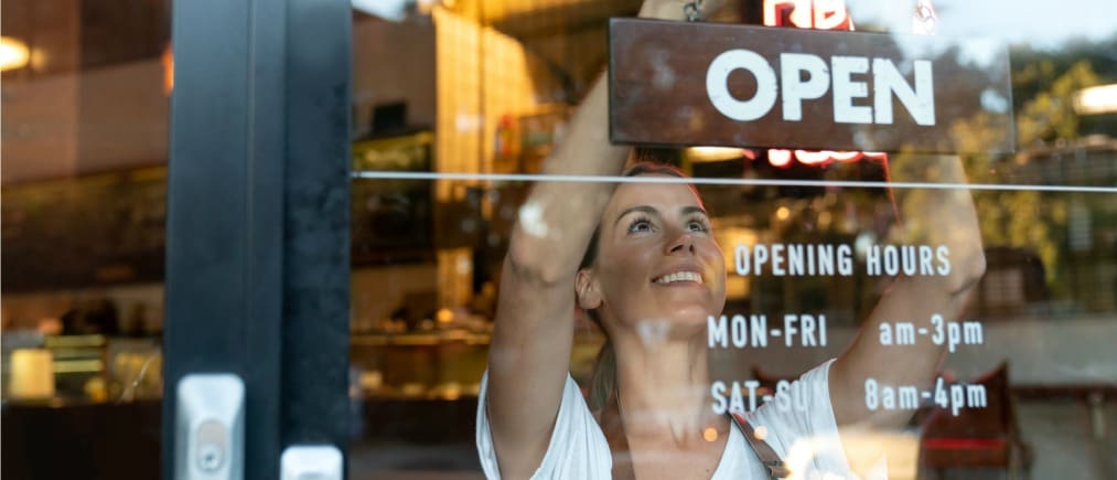 Portrait of a happy business owner hanging an open sign on the door at a cafe and smiling - food and drinks concepts