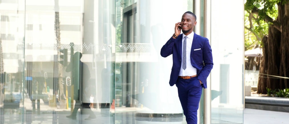 Full length portrait of a happy young businessman walking in the city and talking on mobile phone