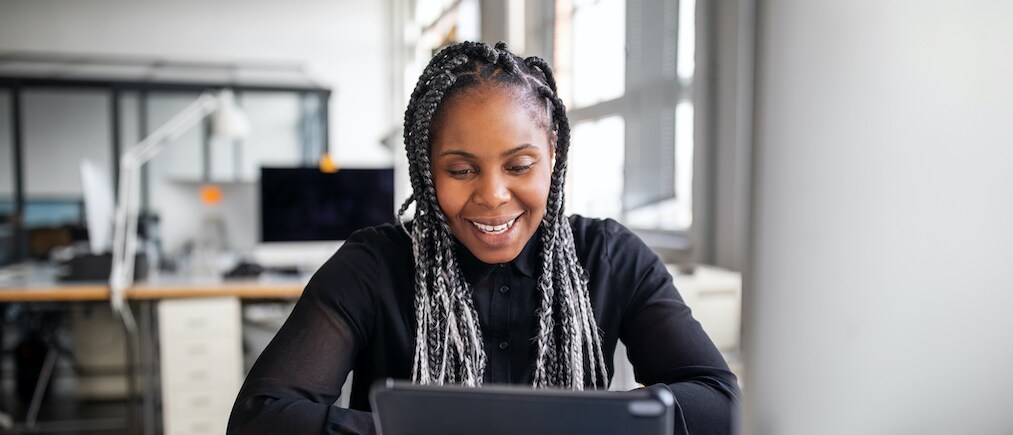 Smiling female executive sitting at her office desk making a video call with digital tablet. African american businesswoman working in office having a video conference.