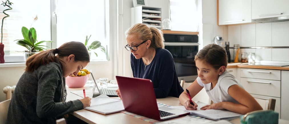Mother helping her daughters to finish school homework during coronavirus quarantine. They are using laptop.