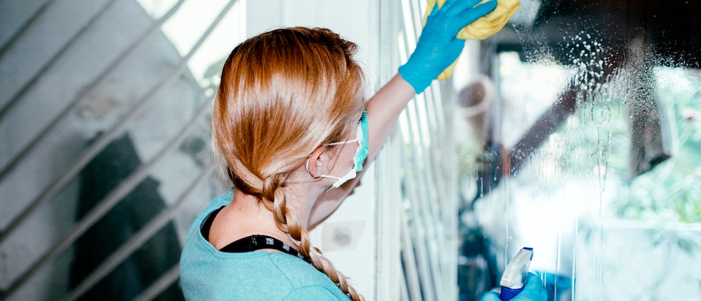 Woman cleaning a door house window with a disinfection spray and disposable wipe. Woman sanitizing home with antibacterial spray. Girl staying at home during coronavirus outbreak