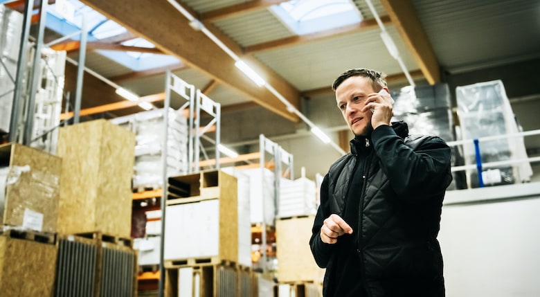 A logistics manager standing in a warehouse talking on the phone to his supervisor.