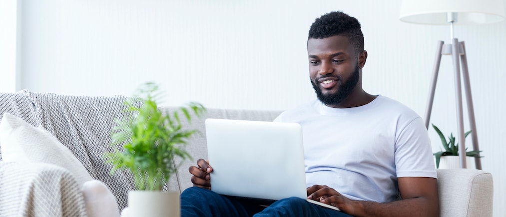 Typing new blog post. African american man blogger using his laptop, sitting on couch at home, copy space
