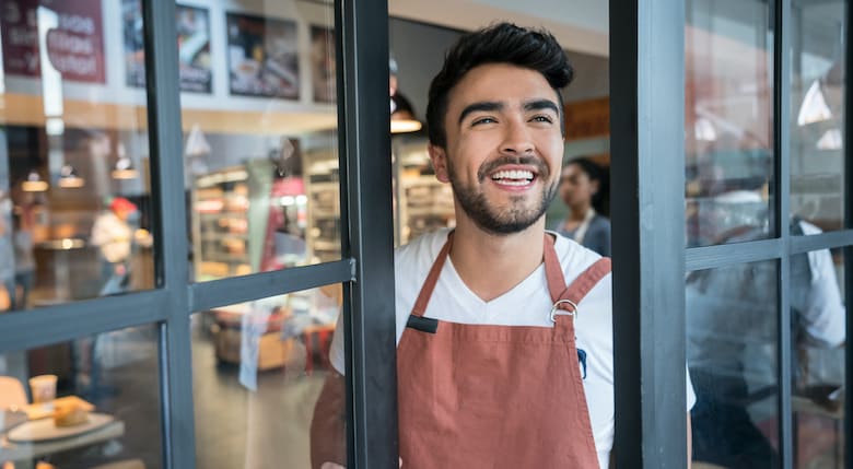 Cheerful business owner of a food store opening the doors for service looking away daydreaming very happy