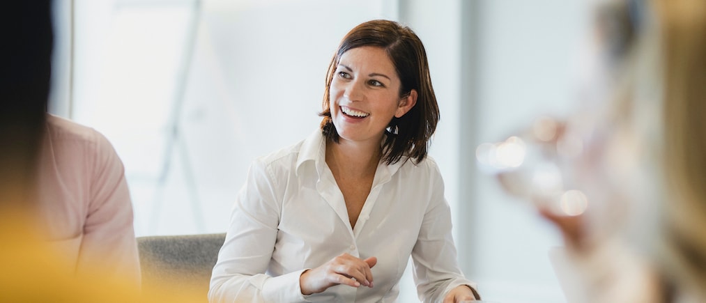 Businesswoman smiling at meeting table, listening, learning, success, happiness