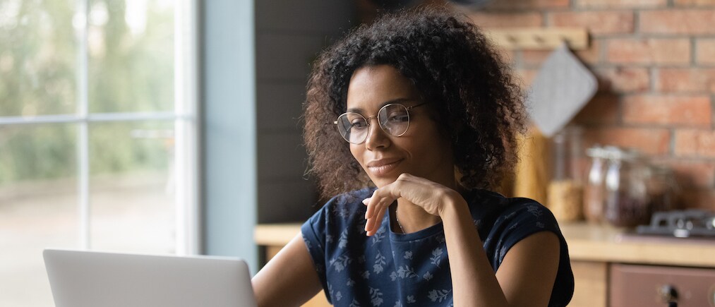 Close up focused African American woman in glasses using laptop, looking at screen, motivated businesswoman or student working on research project online, reading news, searching information