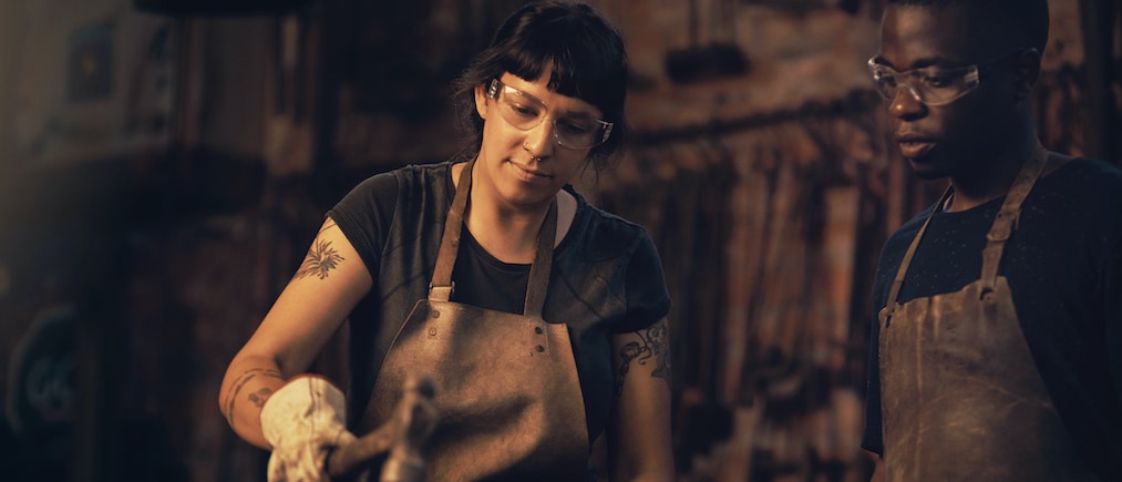 Shot of a young woman hitting a hot metal rod with a hammer in a foundry