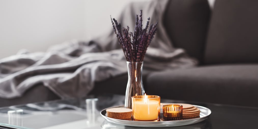 Coffee table design idea: aroma candles and dried lavender bouquet on a metal tray, sofa with grey blanket on background. Simple scandinavian home decor. Hygge concept