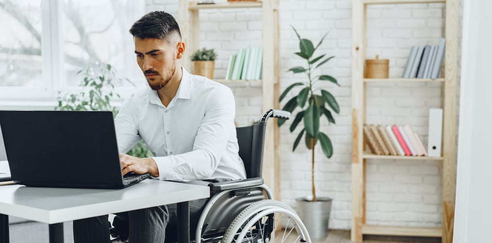 Serious concentrated disabledman in wheelchair using his laptop for work / seeking a job in internet