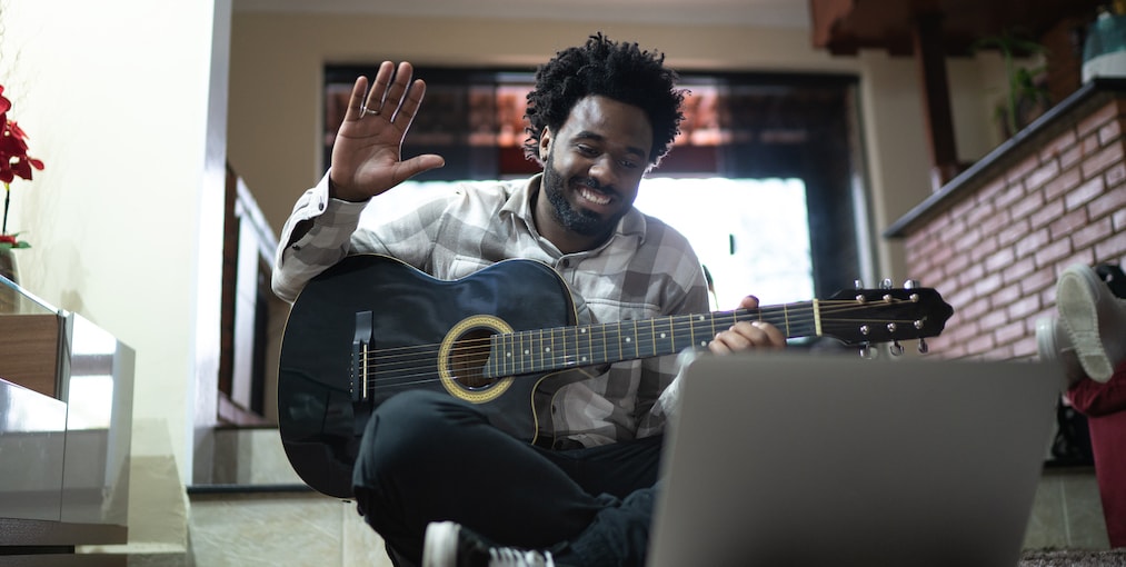 Acoustic guitar teaching through a video call, waving to laptop