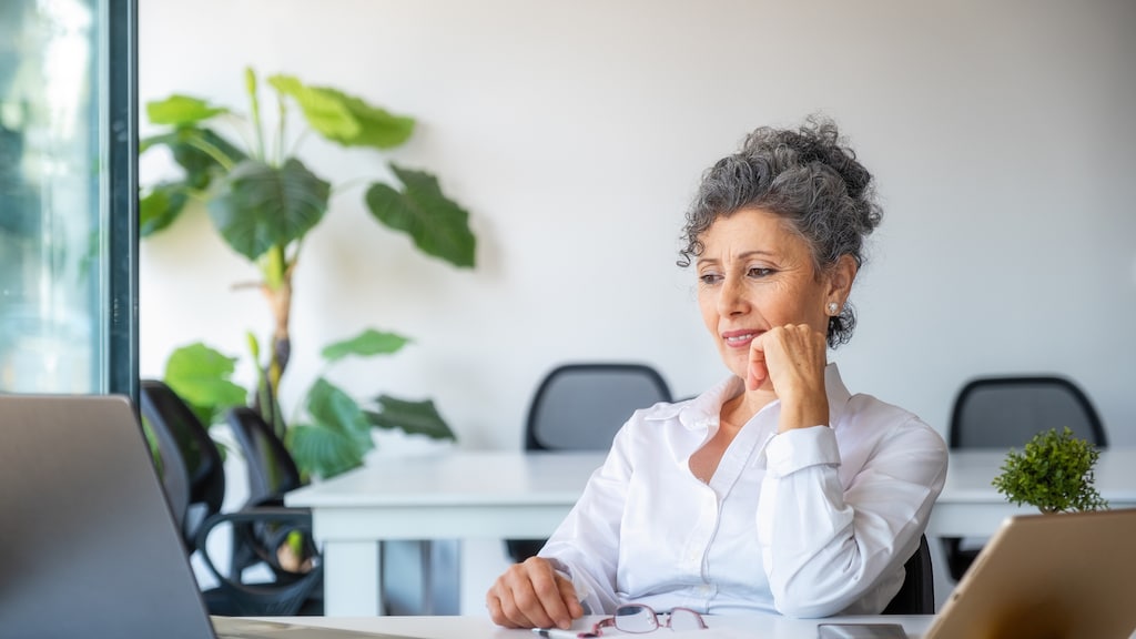Senior gray haired woman looking at computer in office