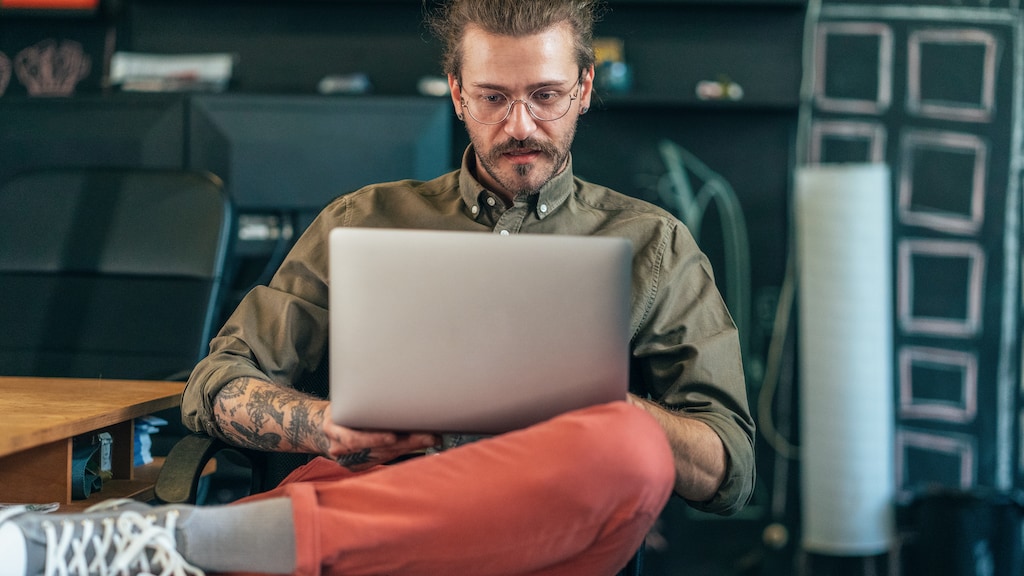 Young modern businessman using laptop at the office. Man with tattoos working in modern creative office.