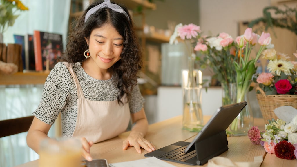 Confident smiling Asian female florist analyzing business performance on tablet reporting a growth in revenue.