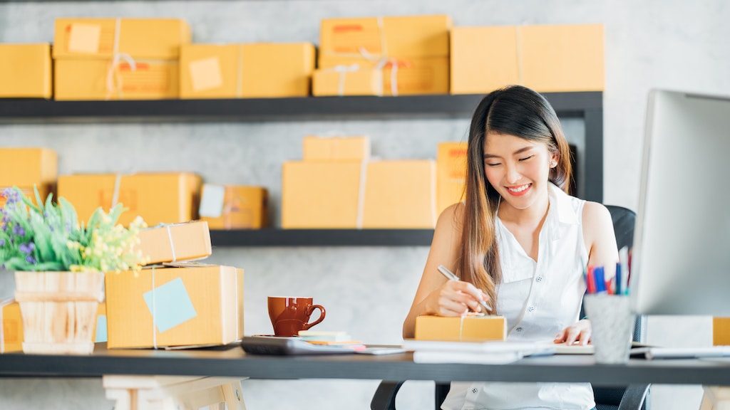 Young Asian small business owner working at home office, taking note on purchase orders. Online marketing packaging delivery, startup SME entrepreneur or freelance woman concept