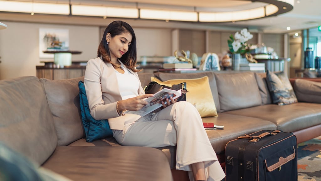 A young and relaxed looking business woman reads a magazine in an airport waiting lounge
