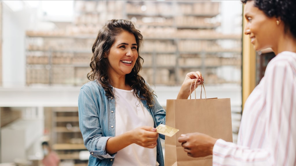 A small business owner smiles at a customer, handing her her credit card and shopping bag