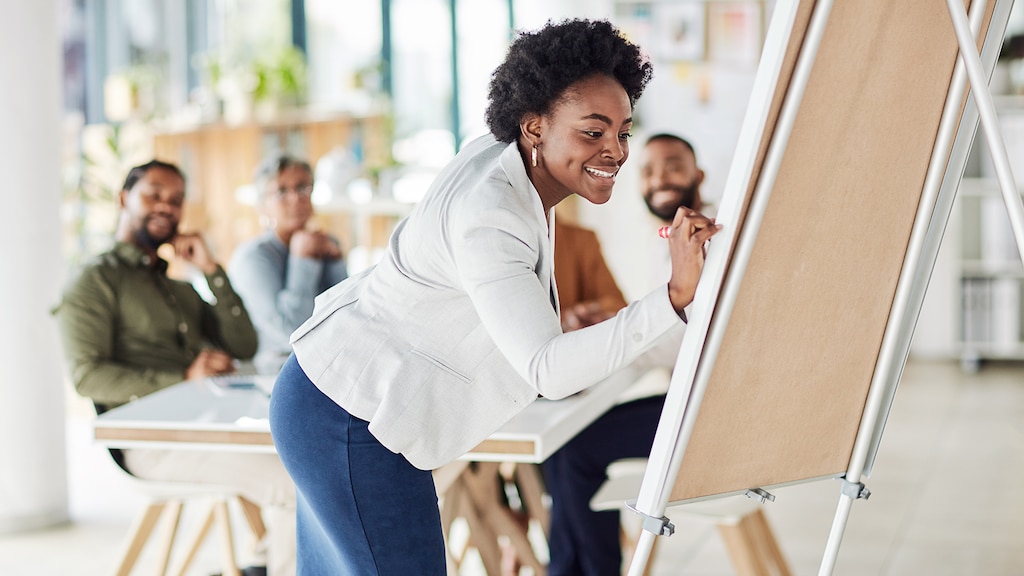 Creative black woman, meeting and writing on Flipchart for team building, coaching or activity at office. Happy African American female in presentation using board to write idea or FAQ for startup