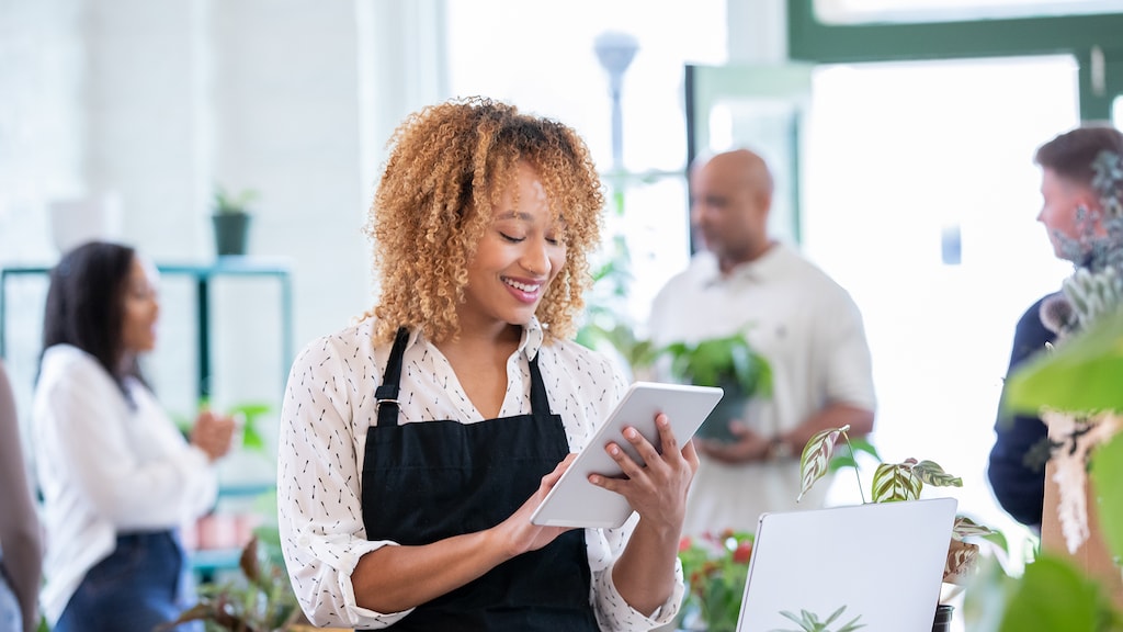 Woman Smiling while looking at Digital Tablet during shift in local gardening store