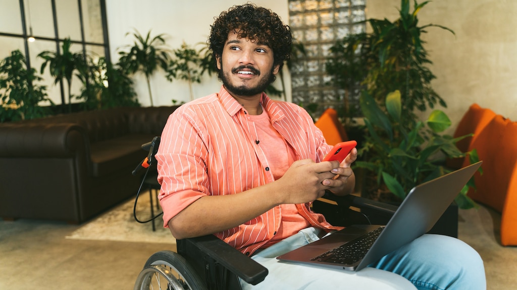 Mixed race Executive Associates Meeting in Office Reception Room and exchanging ideas in sitting area of modern office coworking place. Disabled indian businessman in wheelchair using laptop