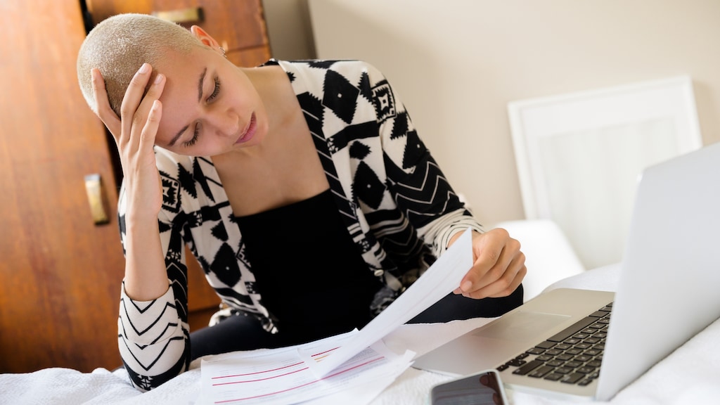 Young woman stressed with paperwork next to laptop and phone