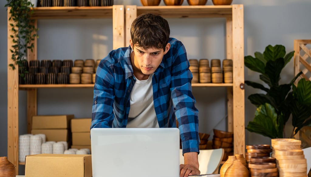Caucasian businessman checking vase goods order for customer on laptop. Young attractive handsome man working to preparing parcel boxes checking ecommerce shipping online retail to sell at home store.