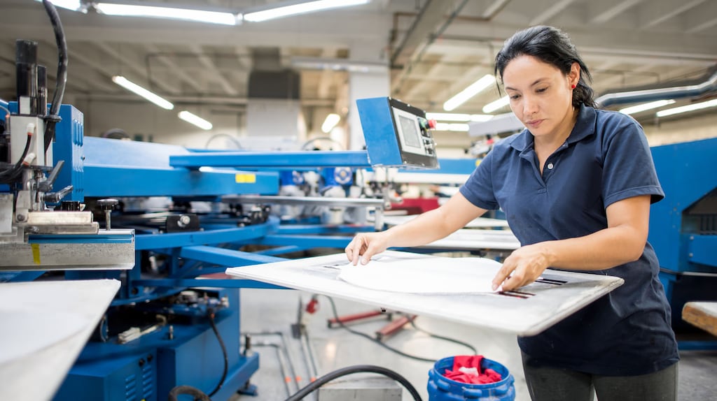 Female worker ironing fabrics at a clothing factory - fashion industry concepts