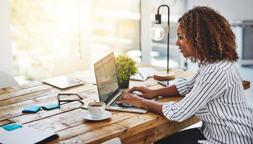 woman in striped shirt with coffee working at computer