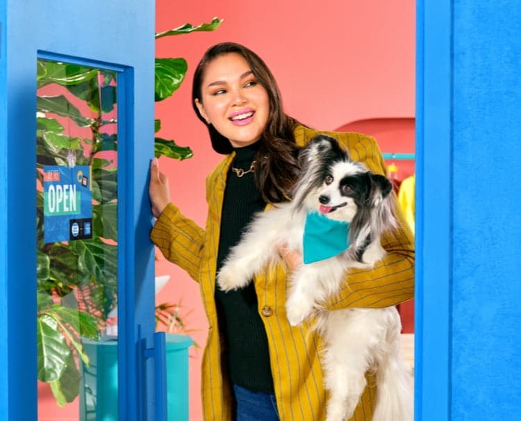 A business owner opening her shop, holding her puppy and smiling for the day ahead