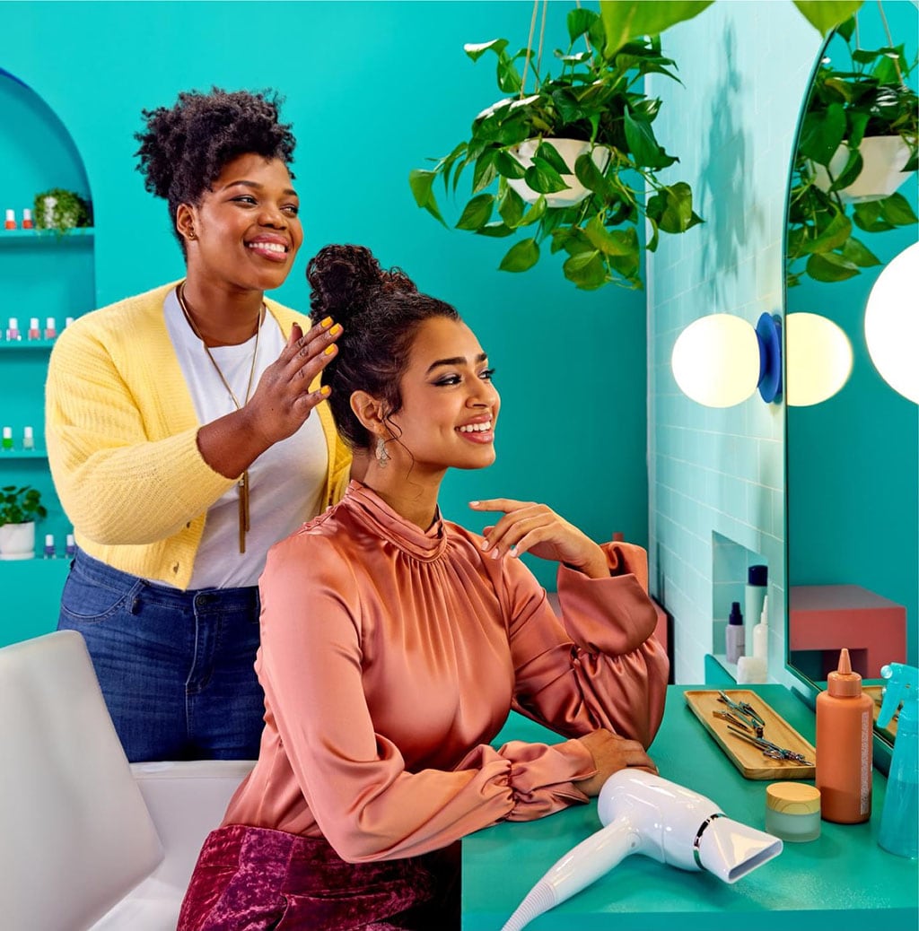 Hairstylist fixing a woman's hair up-do at a salon, woman is checking her hair out in mirror