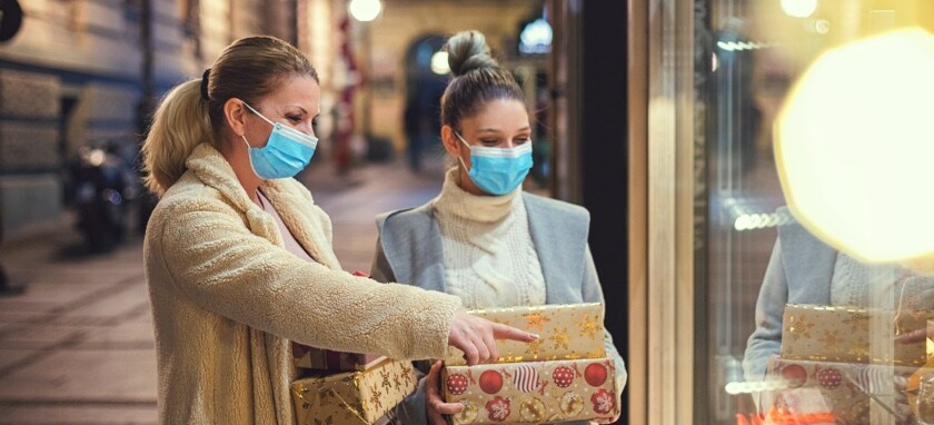 Two woman outside a storefront looking a window display while holding wrapped gifts