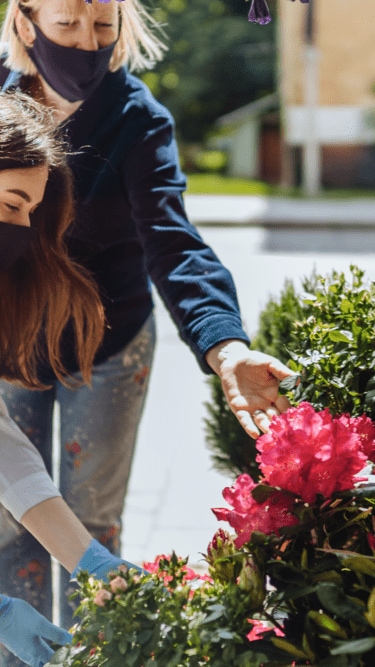 Two women wearing masks interacting with flowers outside